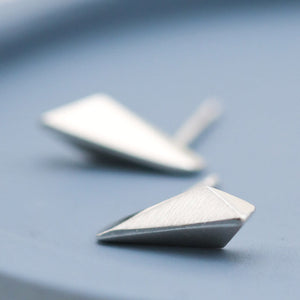 Sterling silver studs with clean Art Deco-inspired geometric lines, small silver stud earrings on a deep blue dish