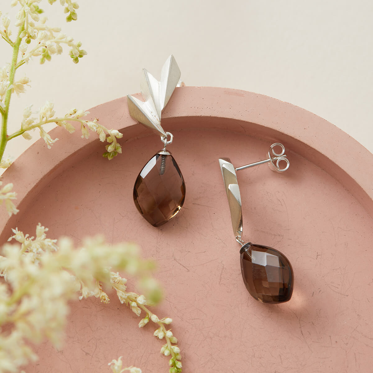 Side-angle view of smoky quartz earrings on a pink dish, capturing the movement of the drop design; timeless art deco statement earrings for elegant gifting.
