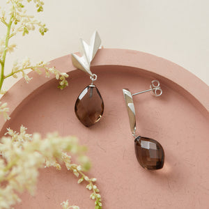 Side-angle view of smoky quartz earrings on a pink dish, capturing the movement of the drop design; timeless art deco statement earrings for elegant gifting.
