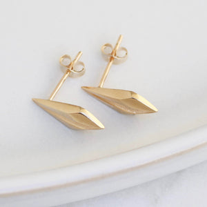 Minimalist gold geometric earrings laid on pale grey, luxury art deco gift for special occasions.
