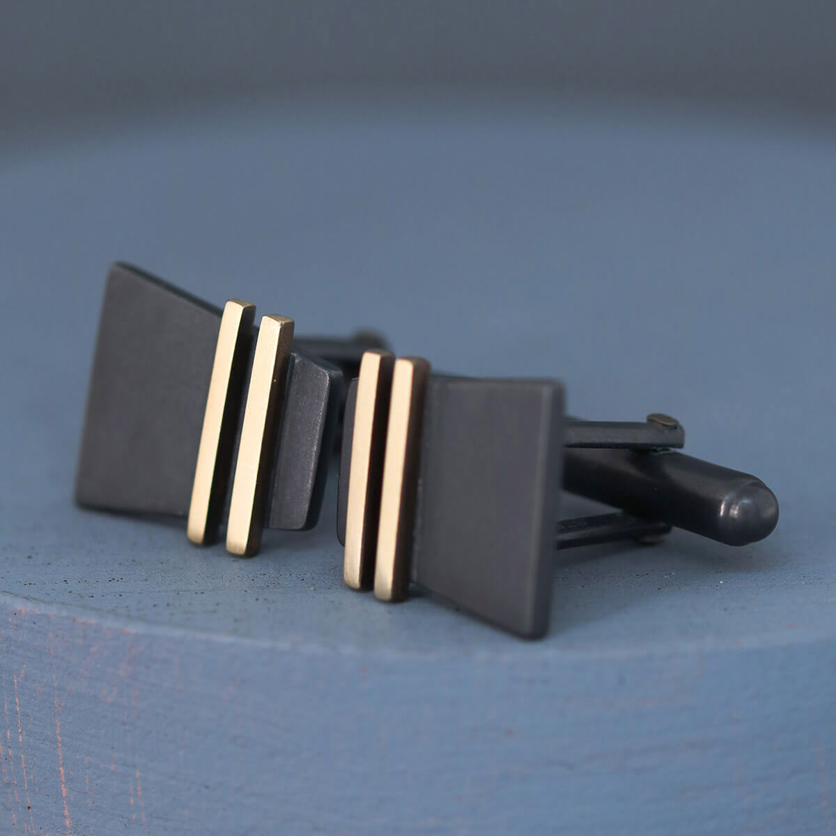 Macro shot of Black and Gold cufflink face on deep blue background, highlighting geometric Art Deco influence, a thoughtful special cufflinks gift for him.