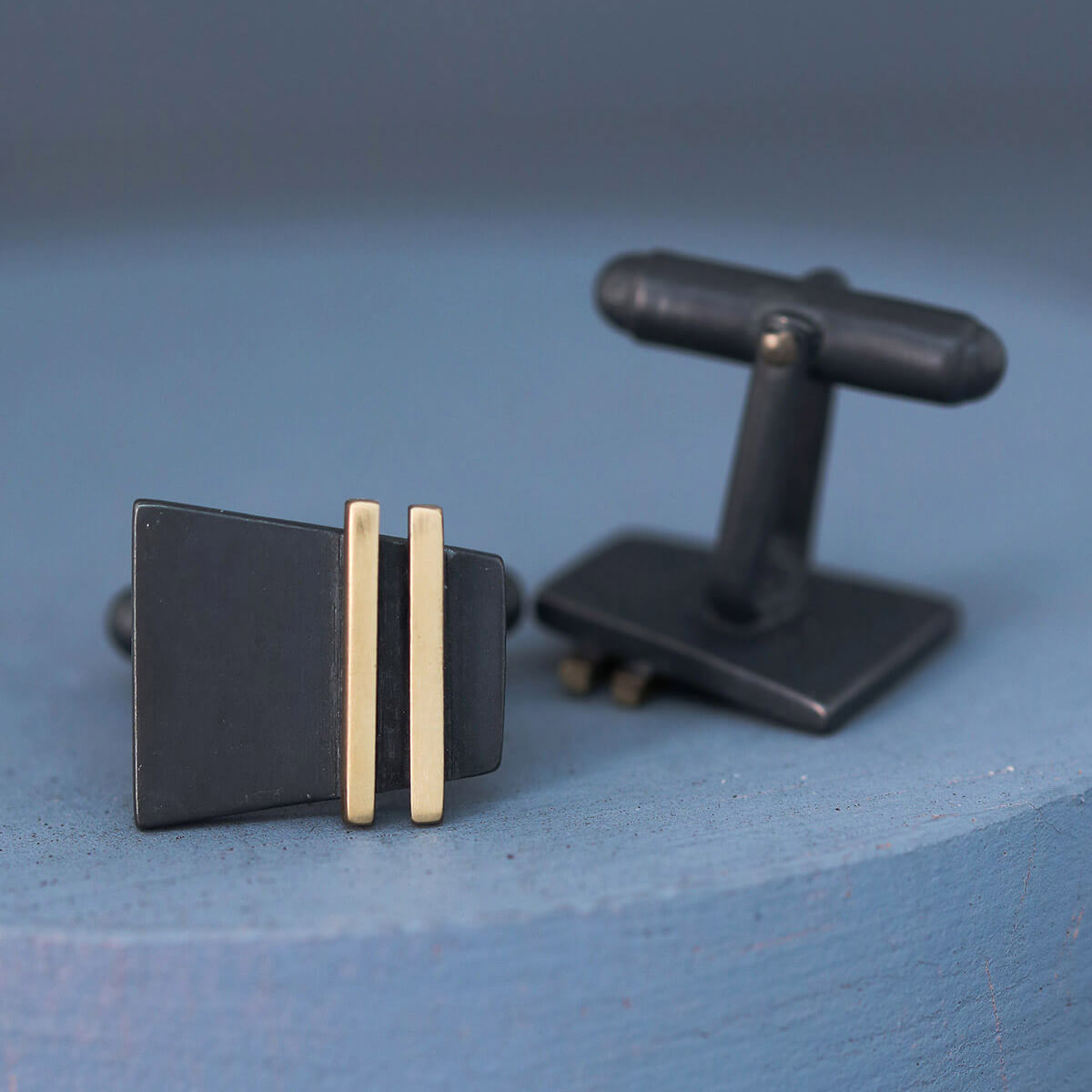Close-up of Black and Gold cufflinks on deep blue backdrop highlighting oxidised silver and 9ct gold stripe, ideal special cufflinks for the groom.