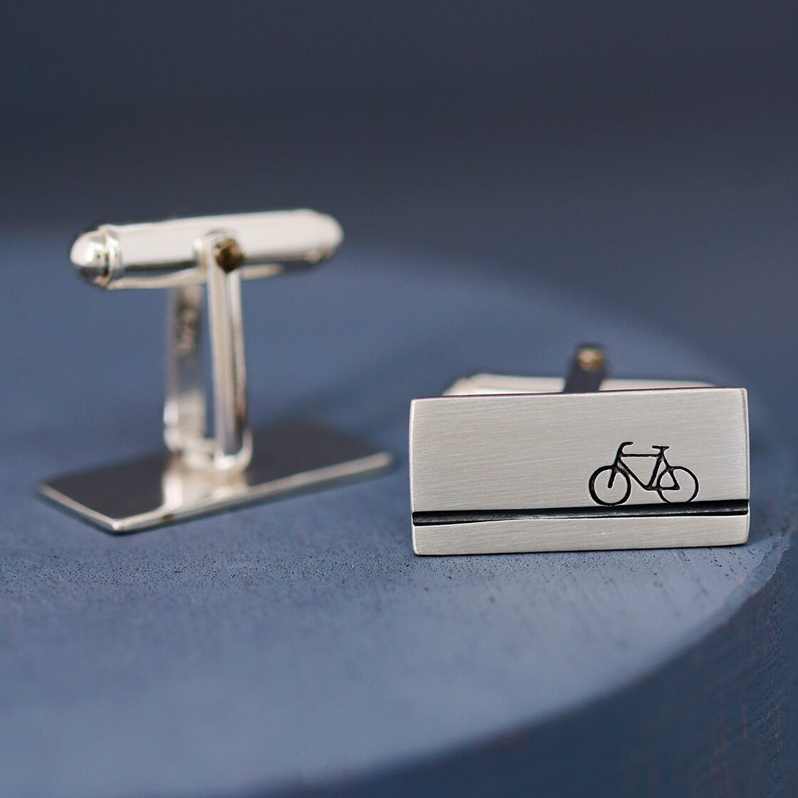 Cycling cufflinks lying flat on a deep blue background, subtle and stylish gift for bicycle lovers or graduation gift for a cyclist starting a new job.