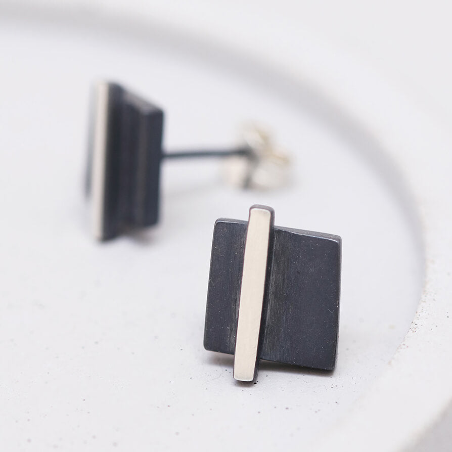 Silver and black earrings laid flat on a grey dish highlighting the geometric shape, perfect thank-you gift.