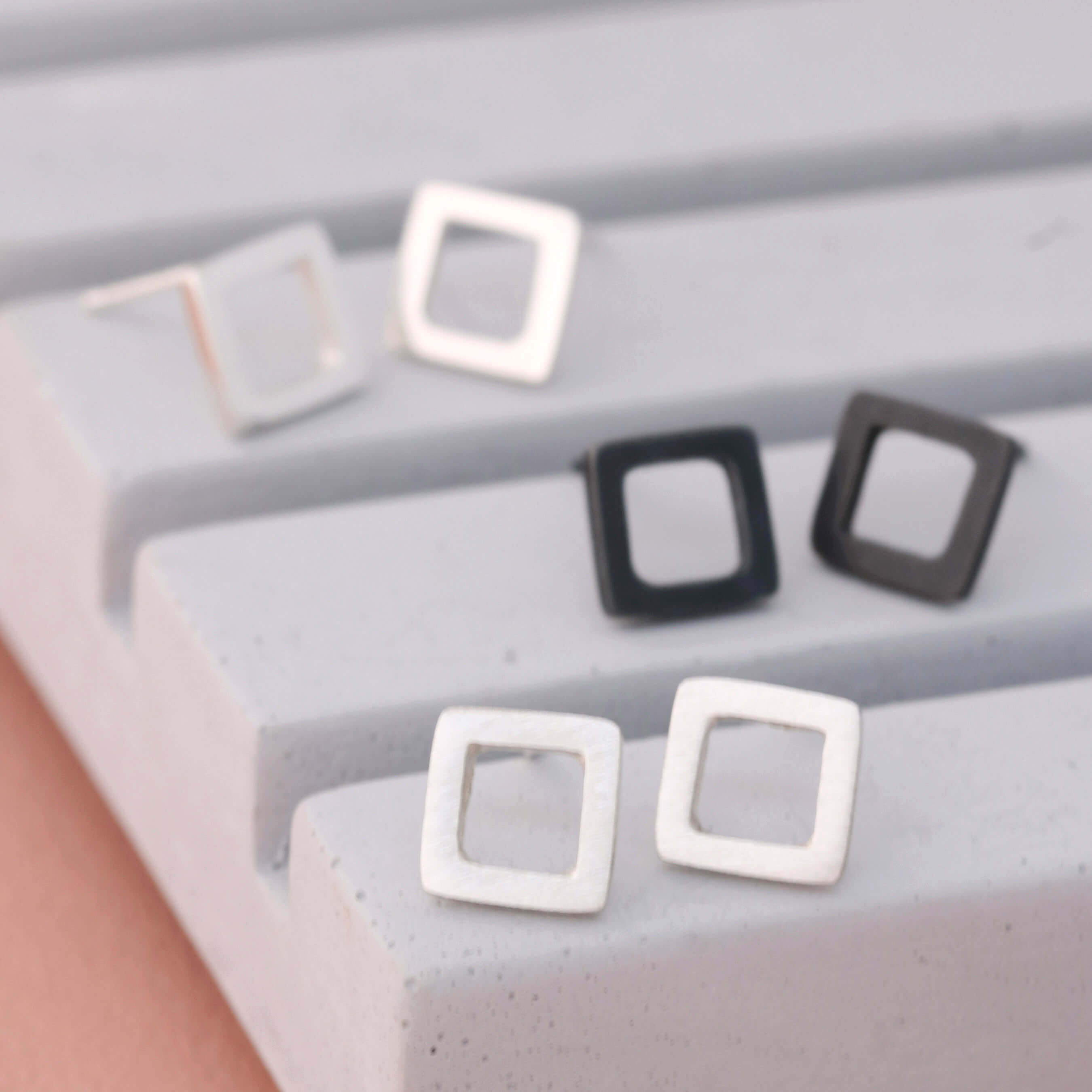 Square silver stud earrings in polished, matte, and oxidised finishes on grey dish
