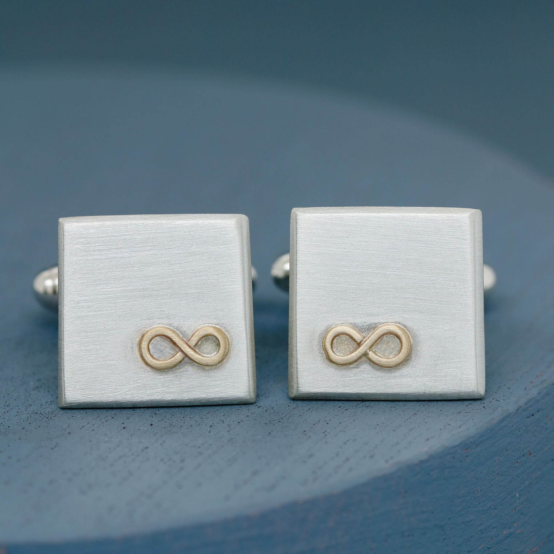 Cufflinks personalised with gold infinity design, pictured slightly offset on a deep blue background – a thoughtful husband anniversary gift.