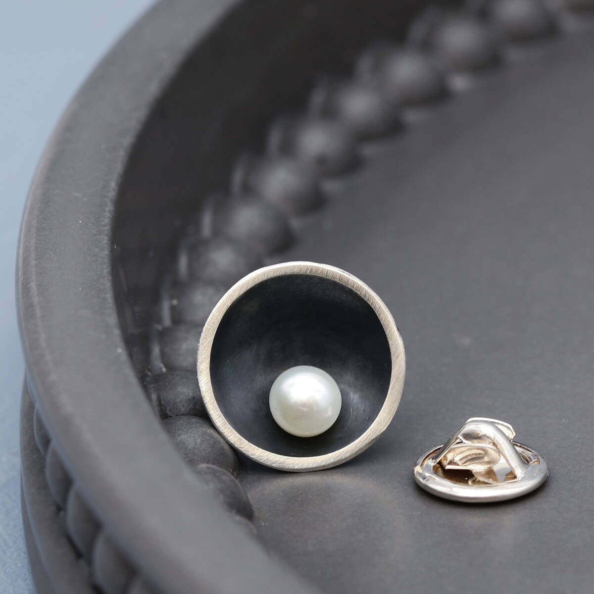 Handmade black pearl tie pin in oxidised sterling silver with a genuine freshwater pearl displayed on a dark grey dish.