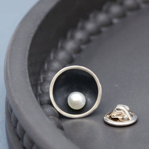 Handmade black pearl tie pin in oxidised sterling silver with a genuine freshwater pearl displayed on a dark grey dish.
