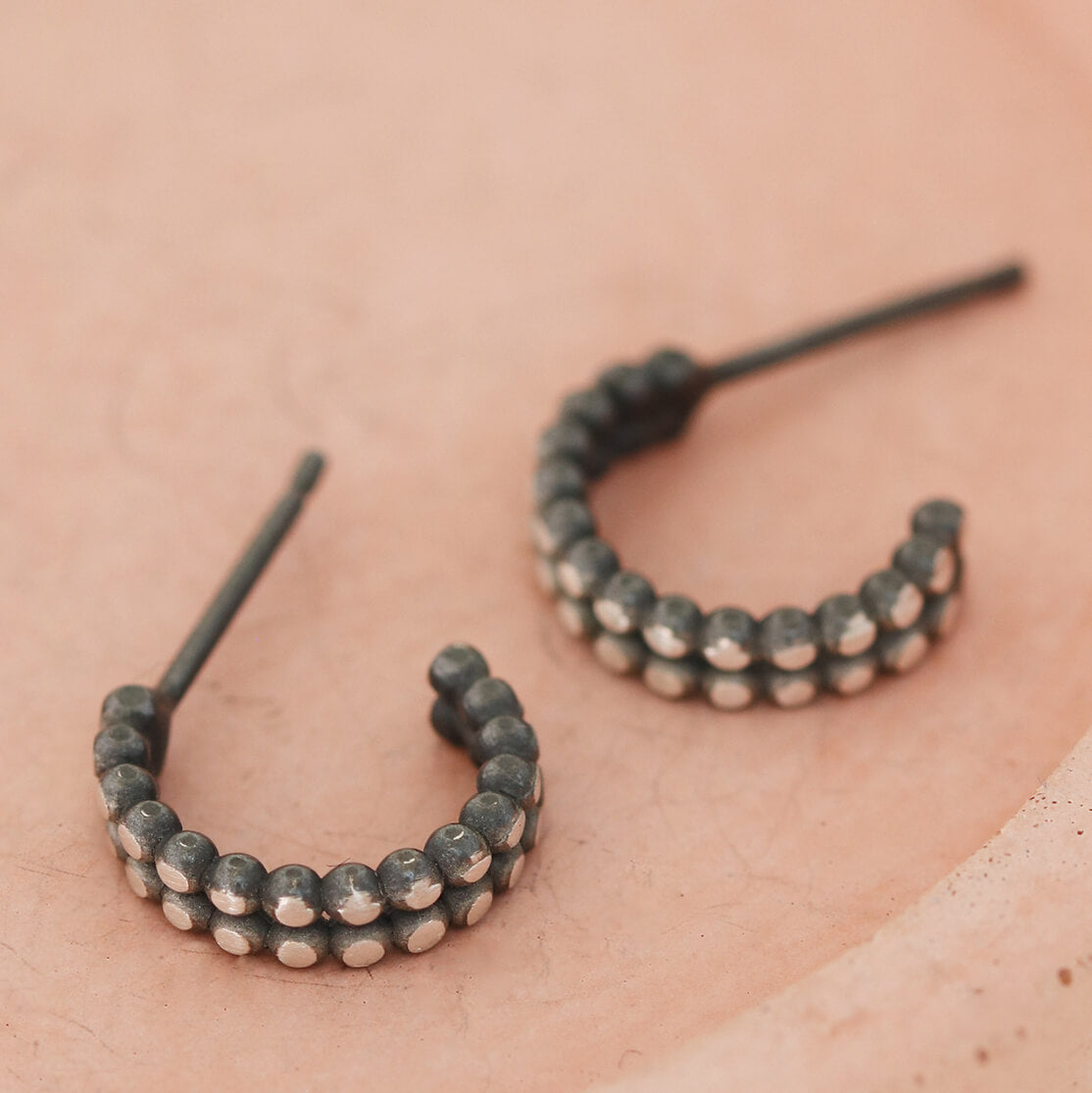 Silver and black hoop earrings displayed on a pink dish, small double hoop design in sterling silver