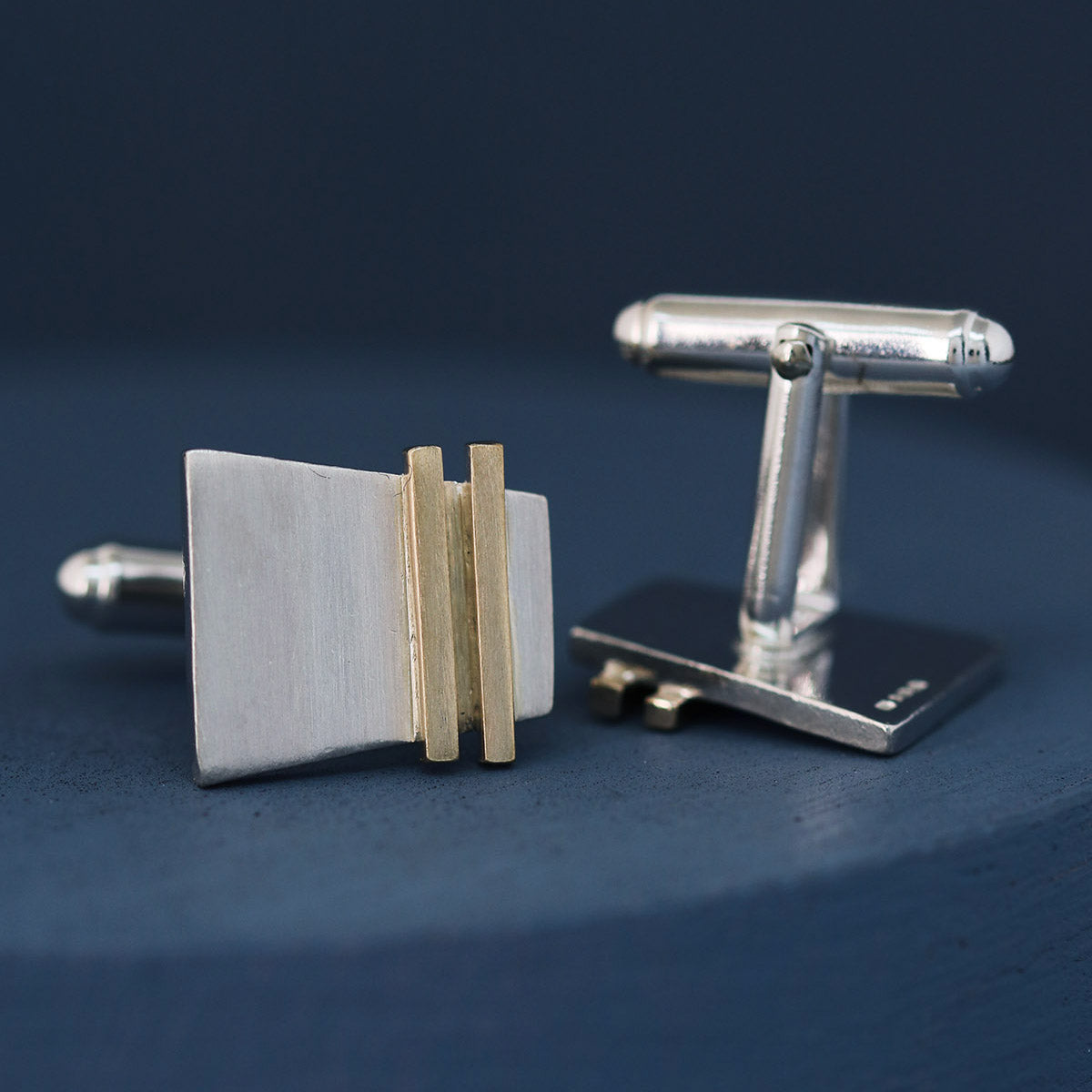 Silver and gold cufflinks displayed on a deep blue background, showing the modern gold pinstripe detail; ideal luxury cufflinks gift for groom or anniversary.