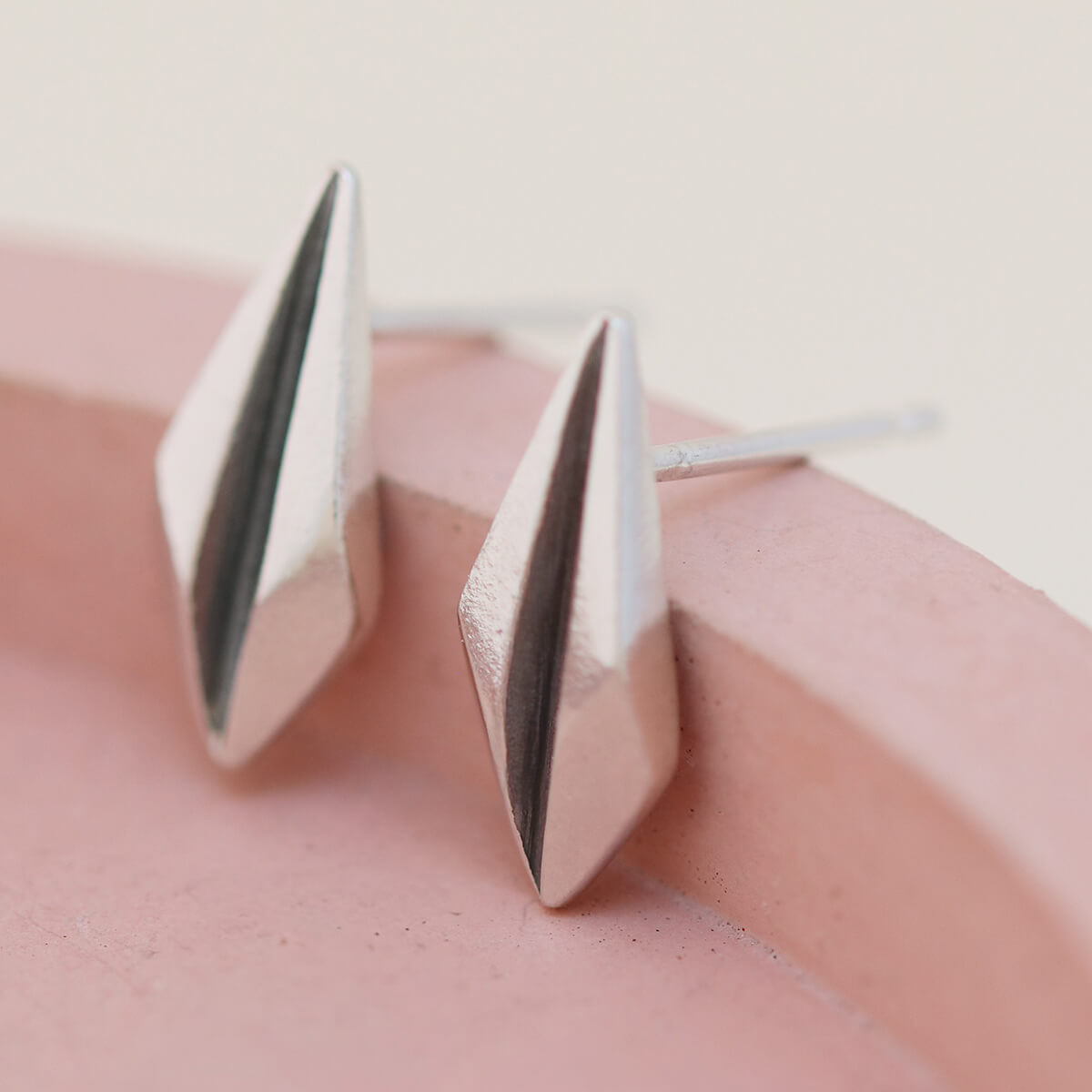 Side angle of art deco earrings studs on pink dish showing depth and clean lines.
