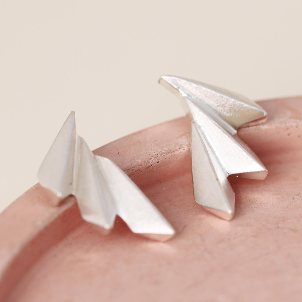 Side angle of art deco fan earrings on a pink dish showing their curved profile.