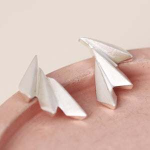 Side angle of art deco fan earrings on a pink dish showing their curved profile.