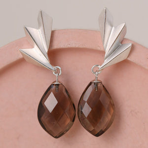 Smoky quartz earrings on a pink dish showing the faceted gemstone and geometric silver fan design; bold art deco statement earrings ideal for gifting.