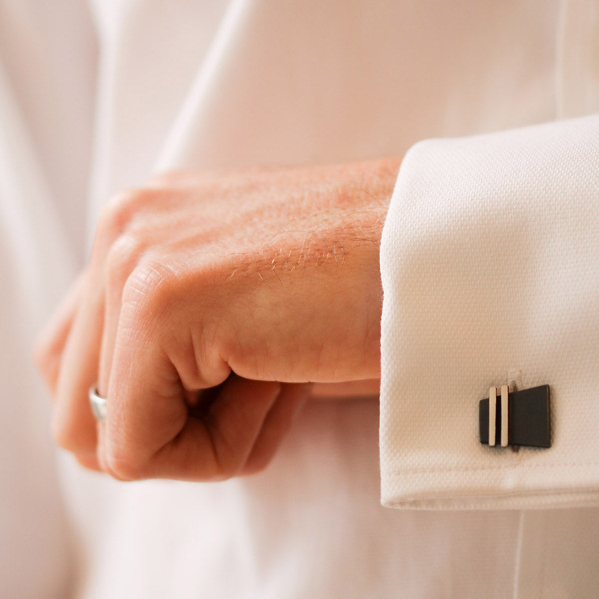 Close-up of a man wearing black cufflinks on a crisp white shirt and dark suit jacket. A timeless and stylish look, perfect as a birthday gift idea for husband or groom.