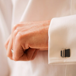 Close-up of a man wearing black cufflinks on a crisp white shirt and dark suit jacket. A timeless and stylish look, perfect as a birthday gift idea for husband or groom.