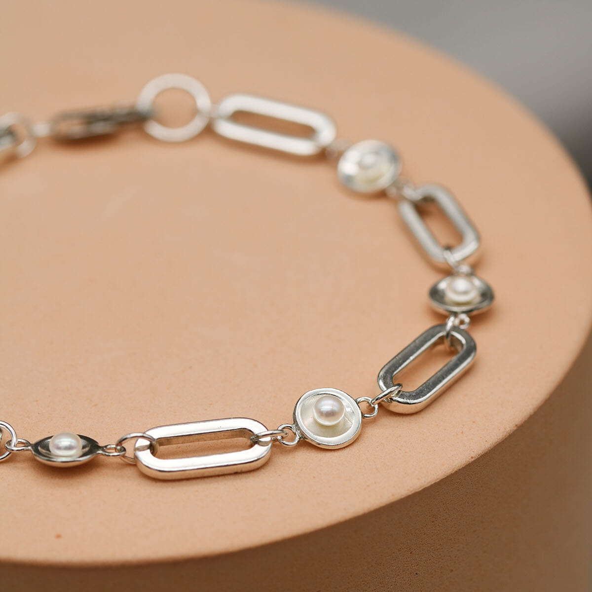 Handmade chunky pearl bracelet in solid sterling silver displayed on a pink plinth against a grey background, showcasing the polished freshwater pearl settings.