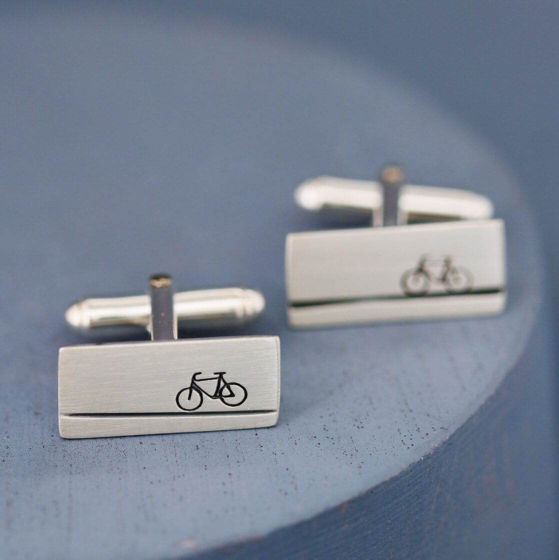 Pair of handmade cycling cufflinks on deep blue background, timeless sterling silver gift for bicycle lovers, cyclists, and sports enthusiasts alike.