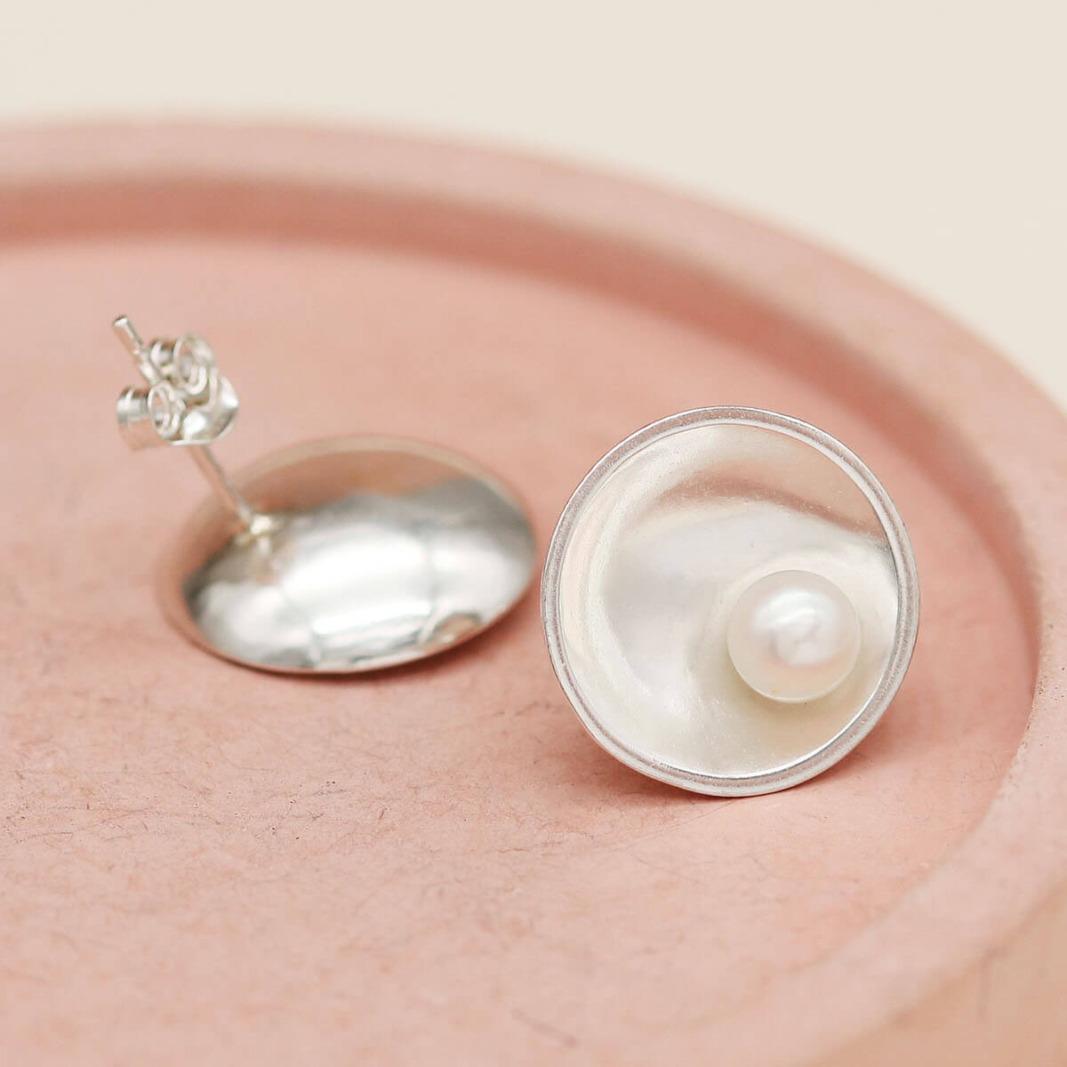Handmade sterling silver pearl stud earrings with genuine freshwater pearls photographed on a pink ceramic dish.
