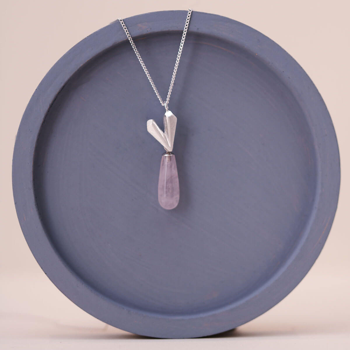 Sterling silver heart necklace on a blue dish, showcasing a pink quartz heart pendant suspended from a fine silver chain.