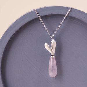 Sterling silver heart necklace with pink quartz heart pendant laid on a blue dish, a delicate handmade heart jewellery design.