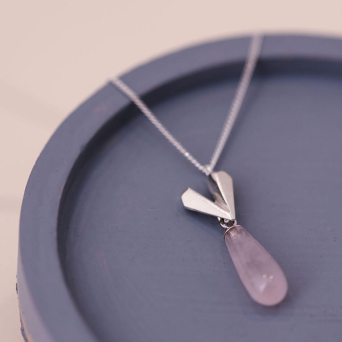 Sterling silver heart necklace styled on a blue dish, featuring a pink quartz heart pendant with a soft blush tone.