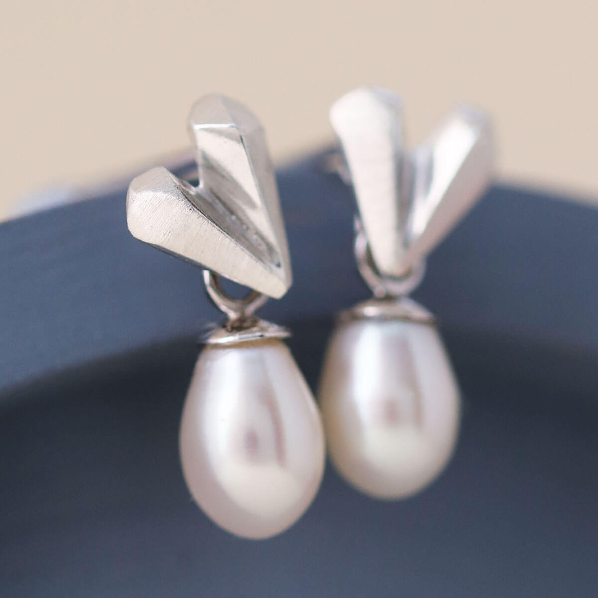 Minimal bridal jewellery image of heart pearl earrings on a blue dish, faceted silver hearts with pearl drops, refined silver wedding earrings