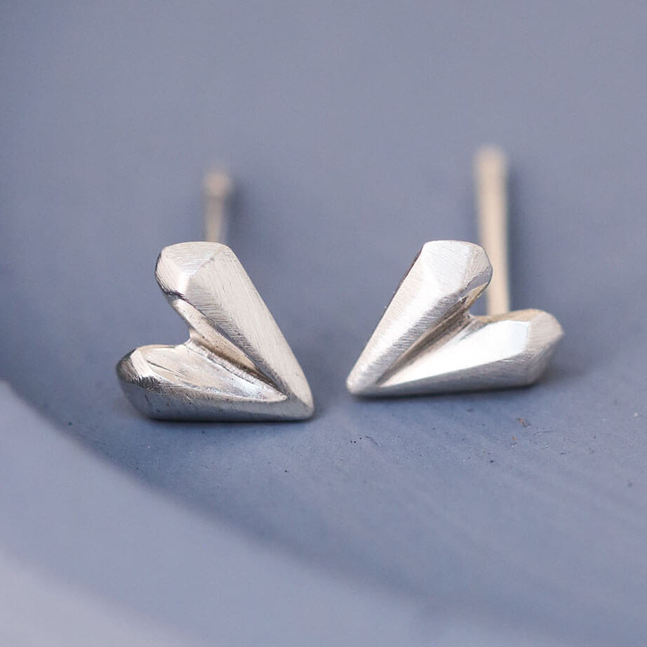 Close up of love heart earrings in sterling silver on blue dish, delicate silver heart stud earrings for second piercings