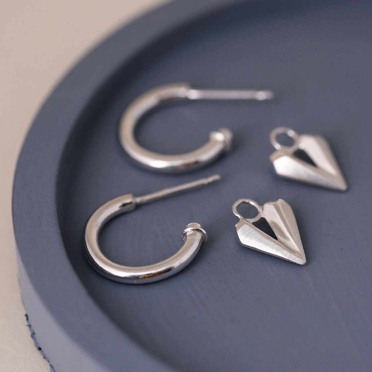 Silver hoop earrings with heart charm on a blue dish, elegant charm hoops with faceted silver heart