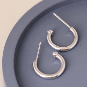 Silver hoop earrings without charm displayed on a blue dish, simple charm hoops worn as plain hoops