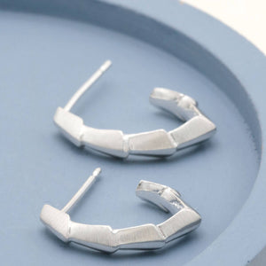 Sterling silver half hoop earrings with an Art Deco-inspired geometric design displayed on a deep blue dish