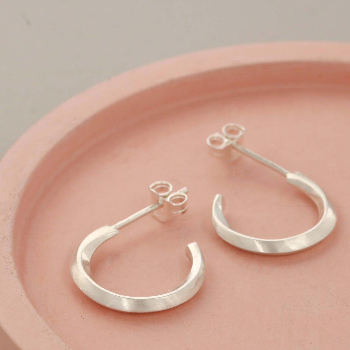Silver hoop stud earrings displayed on a pink dish, handmade sterling silver hoop earrings for women, minimalist everyday jewellery