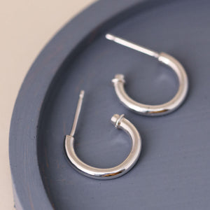 Silver hoop earrings without charm on a blue dish, clean modern hoops with hearts styling option removed