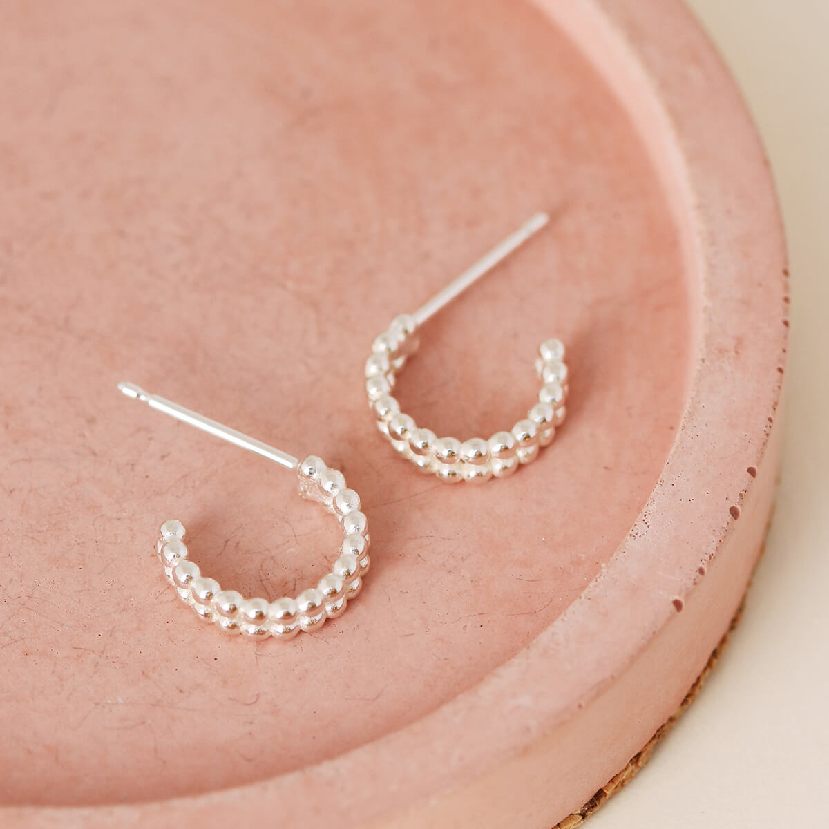 Sterling silver huggie hoop earrings shown flat on a pink dish, classic everyday earrings