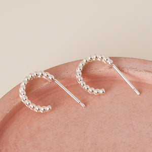 Small huggie hoop earrings in polished sterling silver photographed on a pink dish