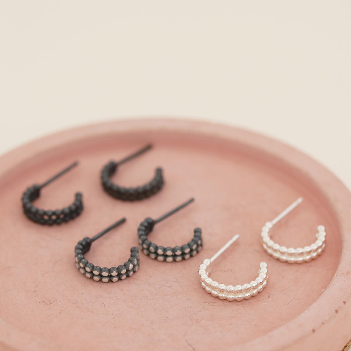 Sterling silver huggie earrings pictured alongside black and silver finishes on a pink dish