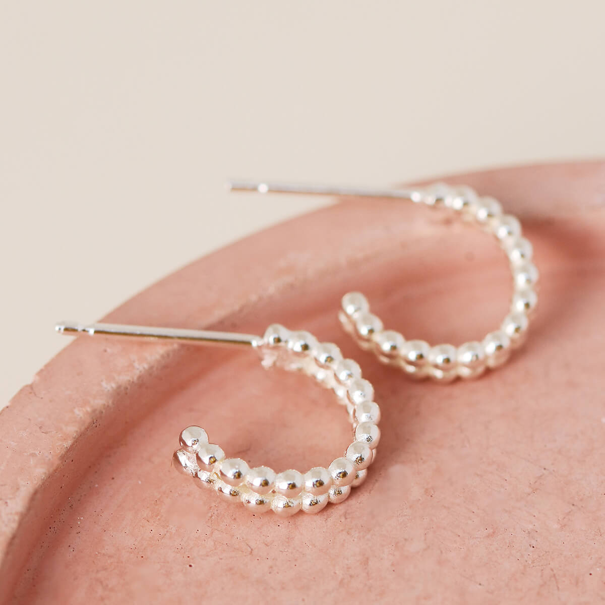 Detail view of sterling silver huggie earrings with double hoop design on a pink dish