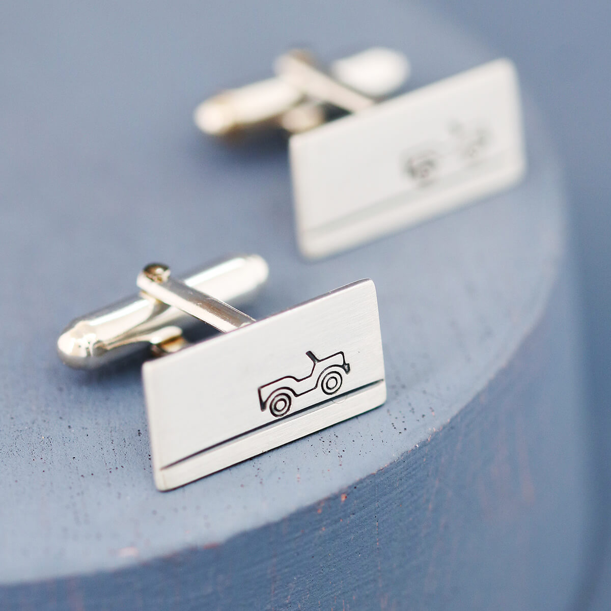 Hand-stamped sterling silver land rover cufflinks photographed on deep blue surface, unique car enthusiast gifts for dad or best man.