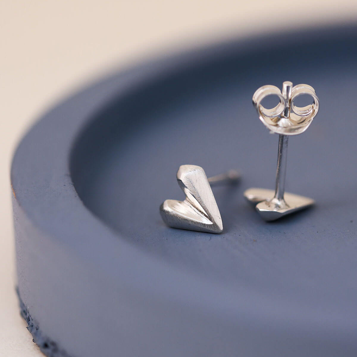 Faceted love heart earrings in solid sterling silver on blue dish, small silver heart stud earrings for teens and women