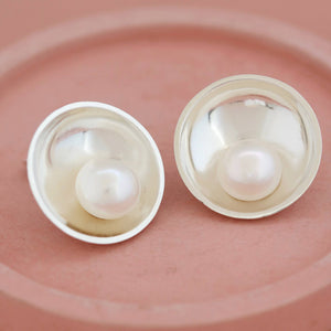 Large statement pearl earrings displayed on a pink ceramic dish