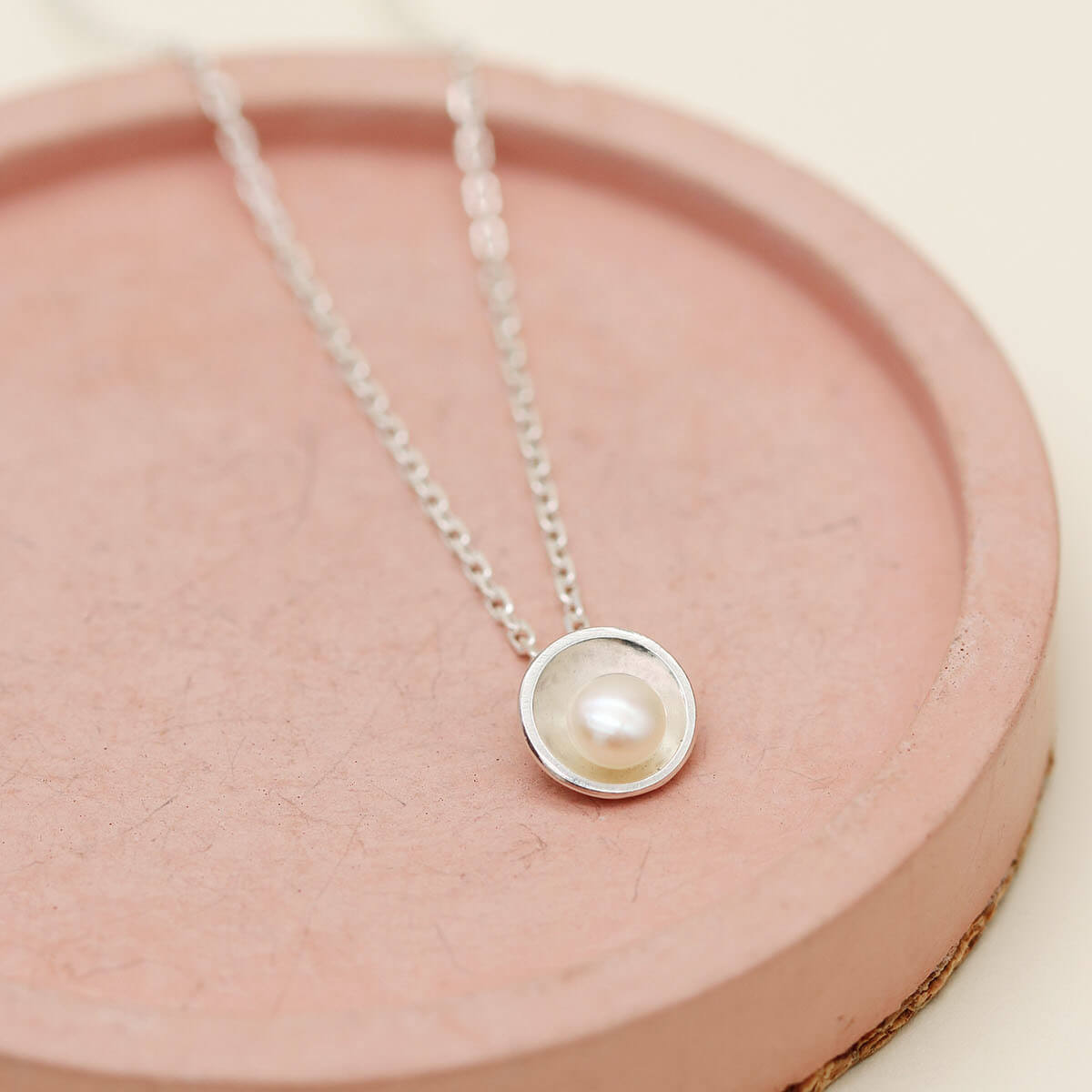 Contemporary sterling silver pearl pendant necklace inspired by Art Deco design, displayed on a pink dish.