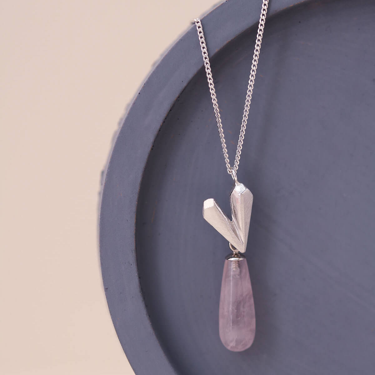 Sterling silver heart necklace styled on a blue dish, featuring a pink quartz heart pendant with a soft blush tone.