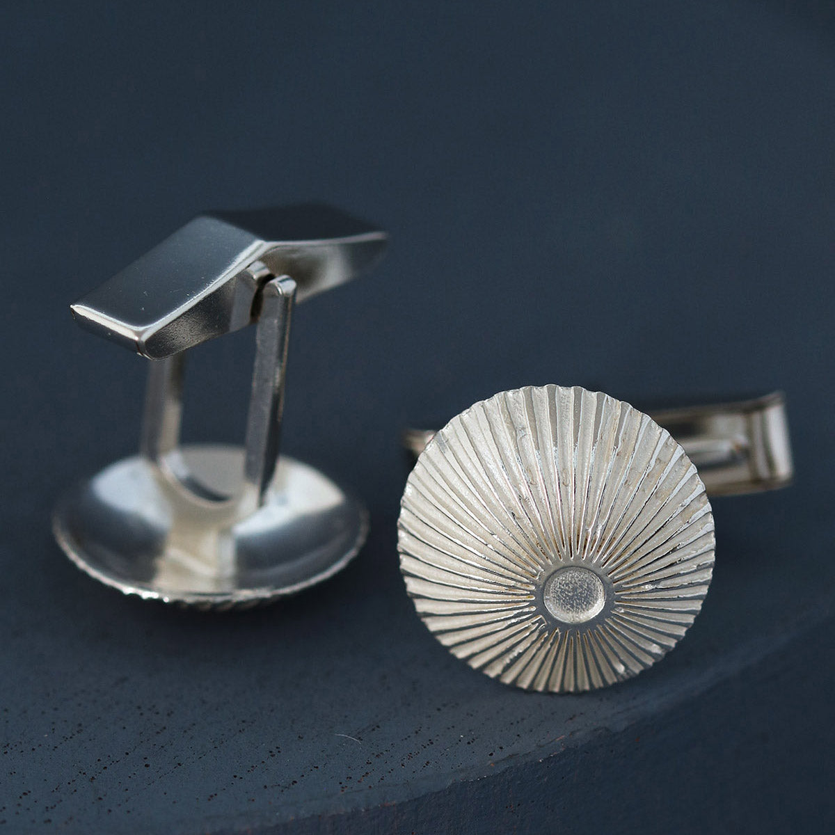 Close-up of round cufflinks in sterling silver showing engraved Art Deco detail on deep blue surface – perfect anniversary gift for him.