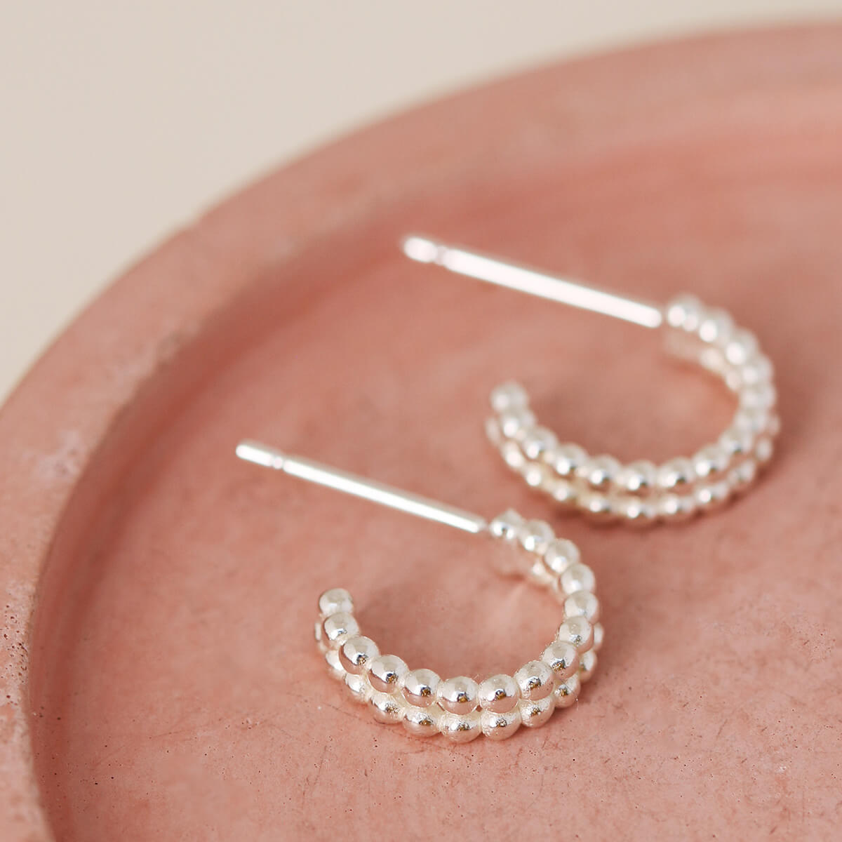 Handmade small huggie hoop earrings in sterling silver presented on a pink dish