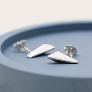 Small sterling silver stud earrings in a geometric kite shape displayed on a deep blue dish, simple everyday silver studs