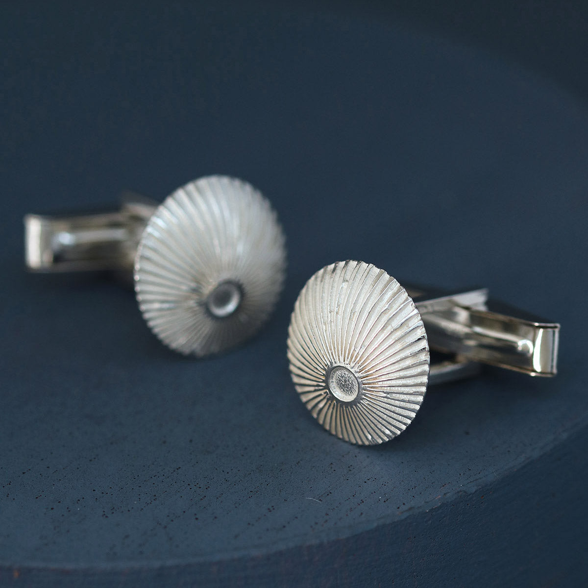 Sterling silver cufflinks angled to show domed round profile and sunburst design on deep blue fabric – perfect luxury corporate gift.