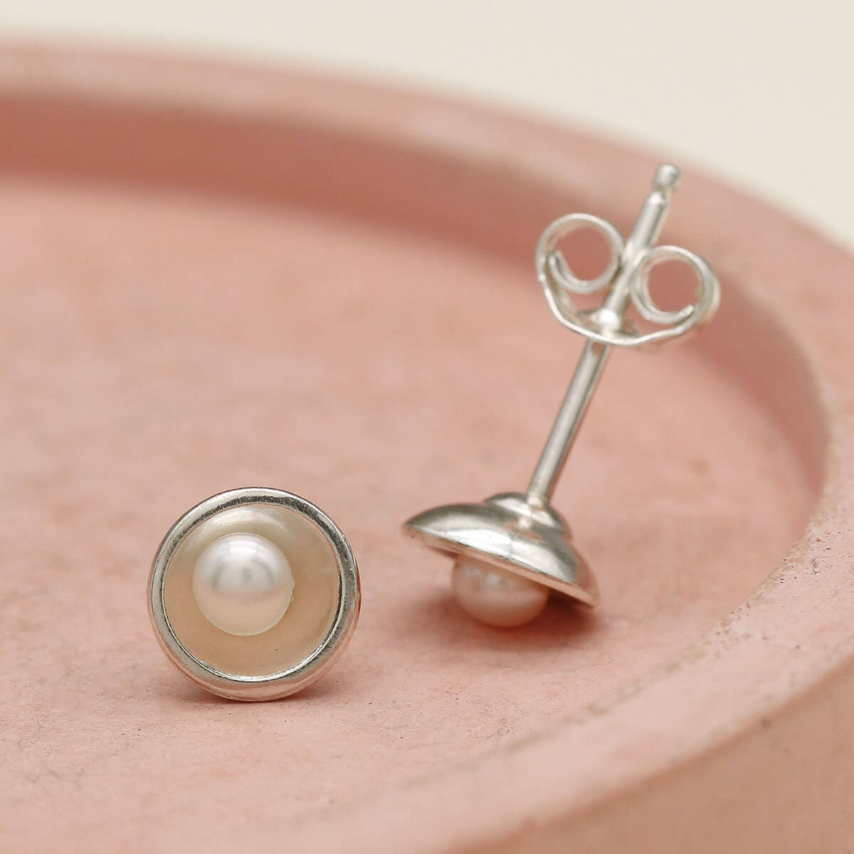 Petite tiny pearl stud earrings handcrafted in sterling silver with genuine freshwater pearls on a pink dish