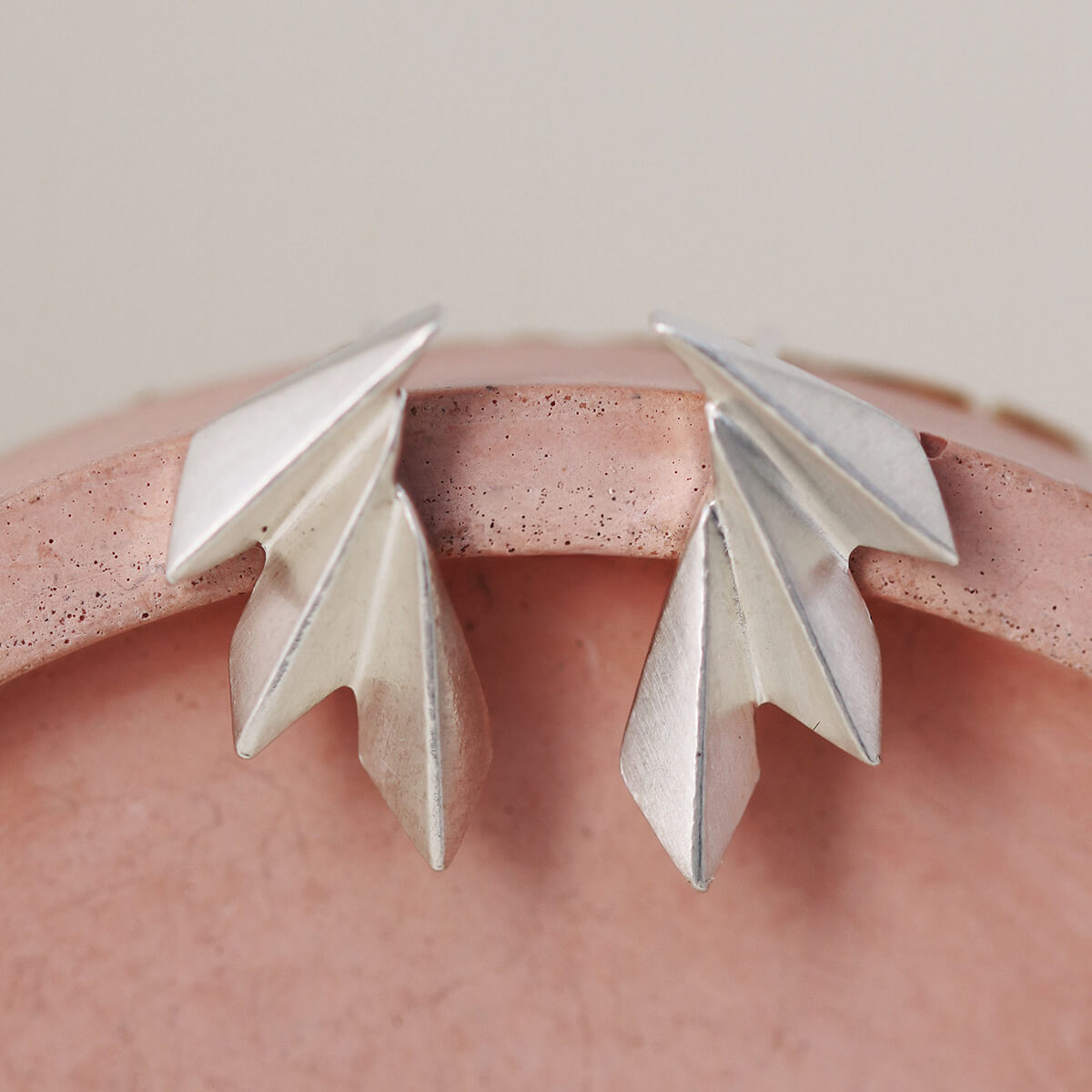 Close-up of art deco fan earrings on a pink dish highlighting the carved silver detail.