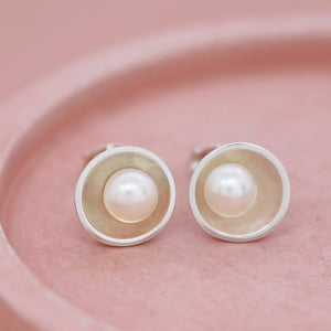 Sterling silver pearl stud earrings placed on a pink dish at an angle, highlighting the reflective polished silver dome and soft lustre of the freshwater pearls.